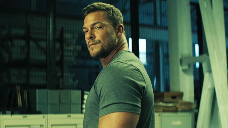 Alan Ritchson's Jack Reacher stands in a warehouse in Reacher