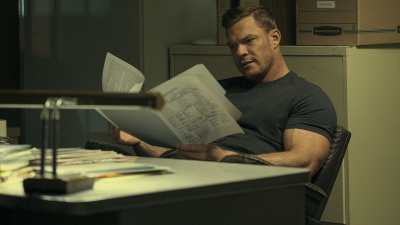 Reacher at a desk reading some papers