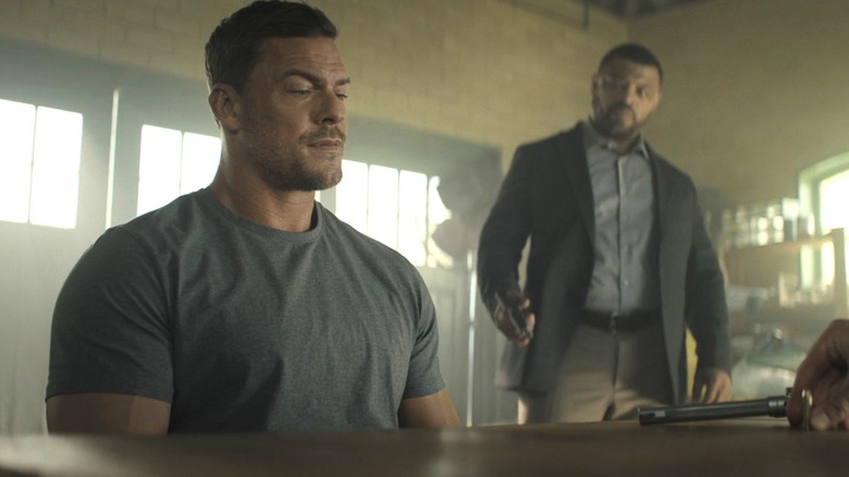 Alan Ritchson's Jack Reacher stares down at a pistol on a table in Reacher