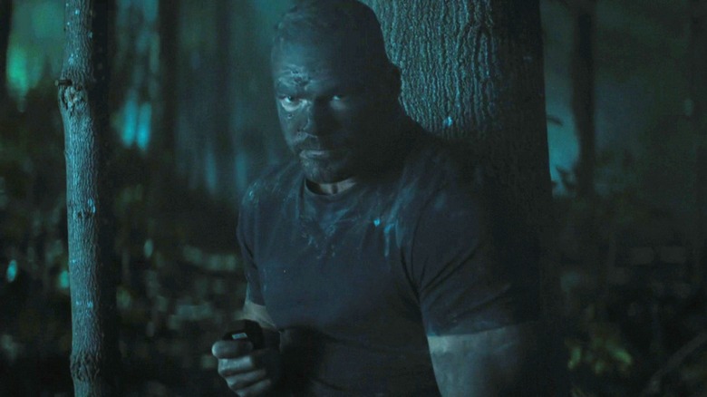 Alan Ritchson's Jack Reacher stands in a forest at night covered in mud in Reacher