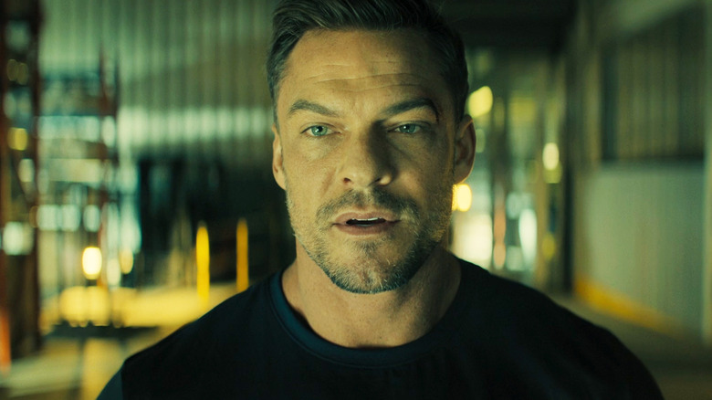 Alan Ritchson as Jack Reacher is seen in closeup standing in a warehouse in Reacher