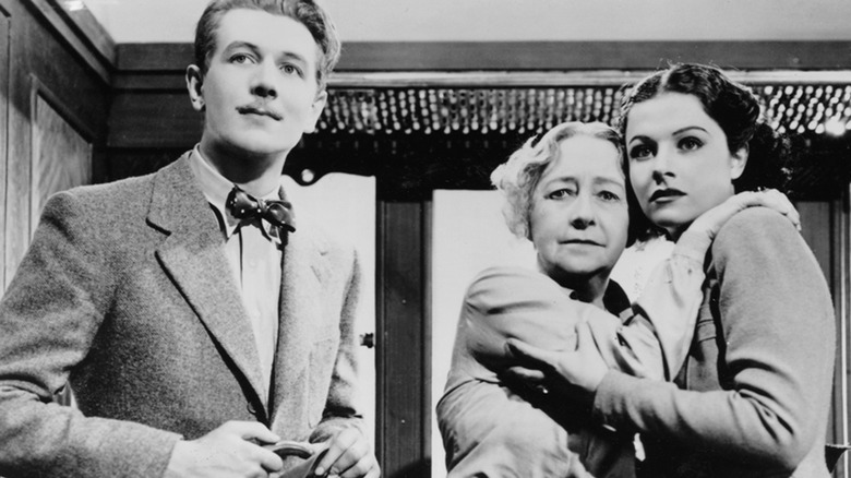 Two scared women clutch each other while a gentleman looks on