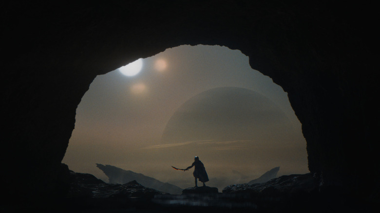 A Yautja holding a blade silhouetted through a cave on a distant planet in Predator: Badlands
