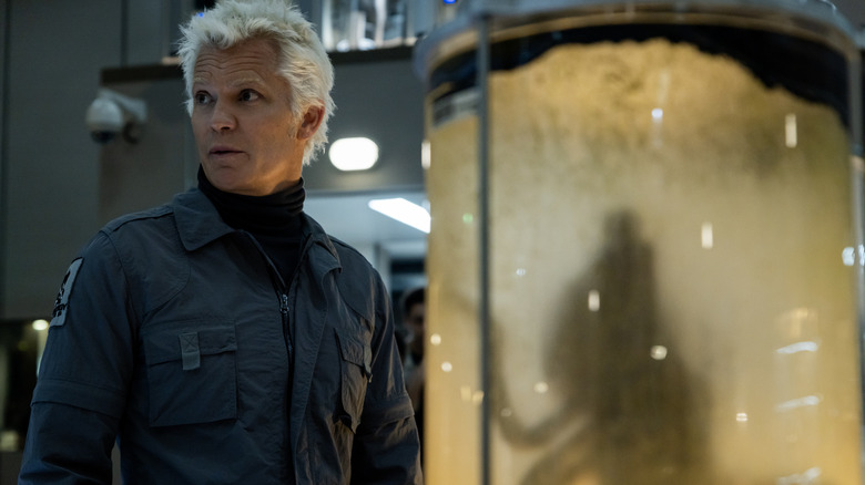Timothy Olyphant as the white-haired Synthetic Kirsh standing next to a container with an alien being inside in Alien: Earth