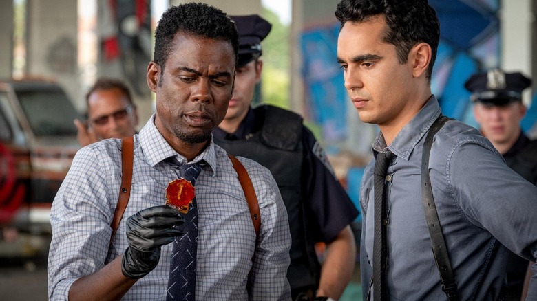 Chris Rock as Zeke Banks and Max Minghella as William Schenk looking at a clue surrounded by cops in Spiral