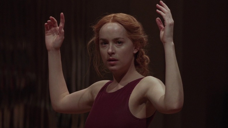 Dakota Johnson as Susanna Bannion, posed with hands raised in Suspiria