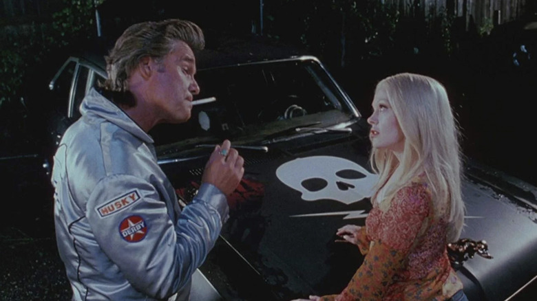 Kurt Russell as Stuntman Mike smoking and talking to Rose McGowan as Pam in front of his matte black 1971 Chevrolet Nova with a skull on the hood in Death Proof