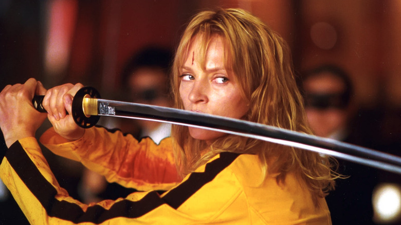 Uma Thurman as Beatrix "the Bride" Kiddo holding her Hattori Hanzo sword while wearing a yellow jumpsuit that's covered in blood in the House of Blue Leaves in front of the Crazy 88s in Kill Bill: Vol. 1
