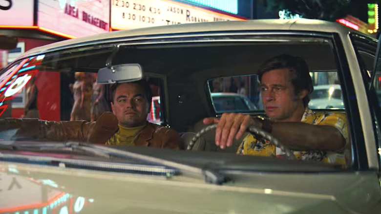 Leonardo DiCaprio as Rick Dalton sitting in the passenger seat of his 1966 Cadillac Coupe de Ville while Brad Pitt as Cliff Booth drives through Los Angeles in Once Upon a Time in Hollywood