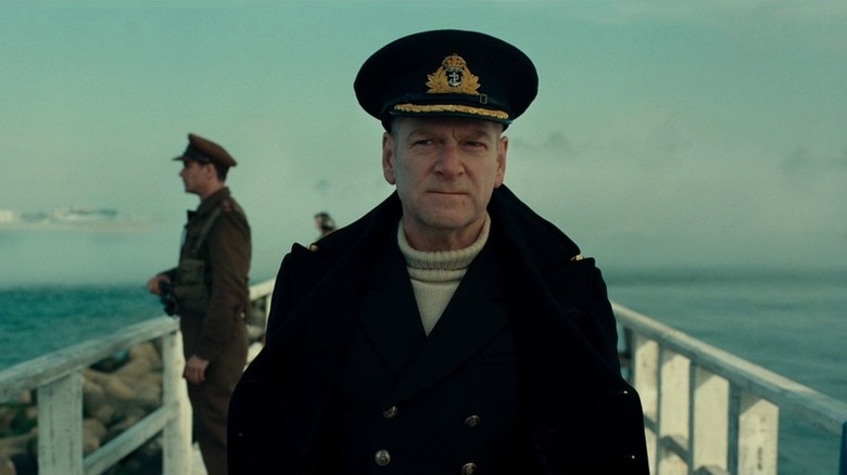 Kenneth Branagh as Commander Bolton, in uniform standing by the sea with another officer behind him as he looks off into the distance behind the camera.