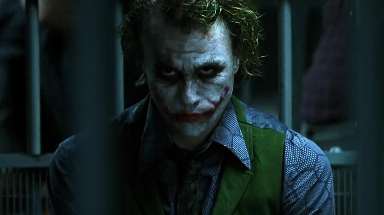 Heath Ledger as The Joker, looking menacingly off behind the camera while in a jail cell.