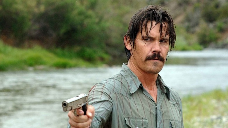 A soaking wet Llewelyn Moss (Josh Brolin) aims a pistol by a river in No Country for Old Men