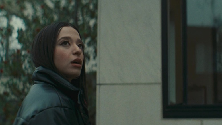Mikey Madison as Ani Mikheeva standing by a guardhouse and looking to her left in Anora