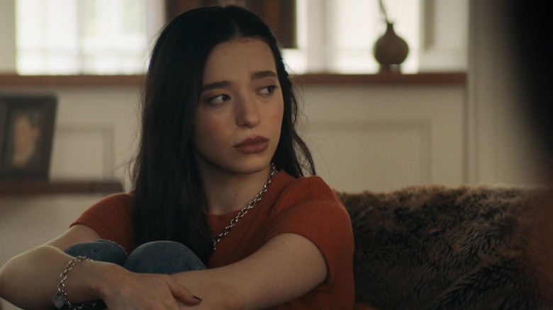 Mikey Madison as Amber Freeman sitting on a couch and hugging her knees in Scream