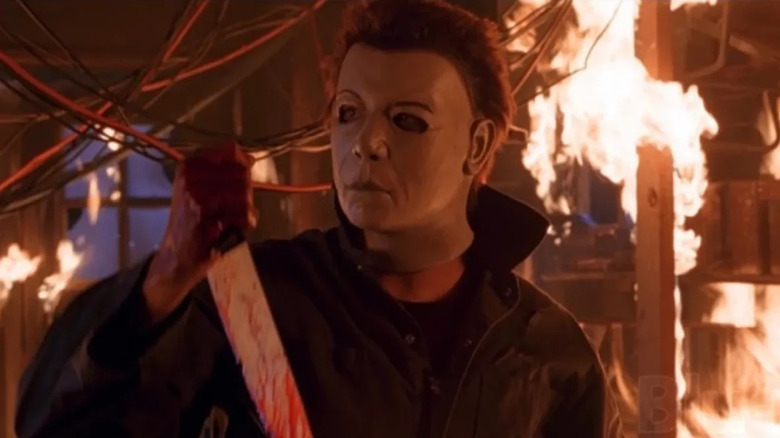 Michael Myers (Brad Loree) holds up a bloody knife in a burning garage in Halloween: Resurrection
