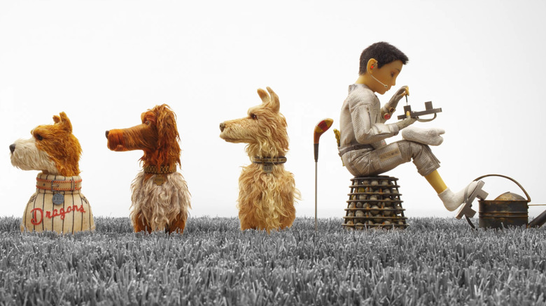 Atari Kobayashi, sitting with three dogs as he tinks with a sandal in Isle of Dogs
