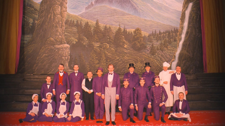 Ralph Fiennes and Tony Revolori as Gustave and Zero, posing with the rest of the hotel staff in The Grand Budapest Hotel