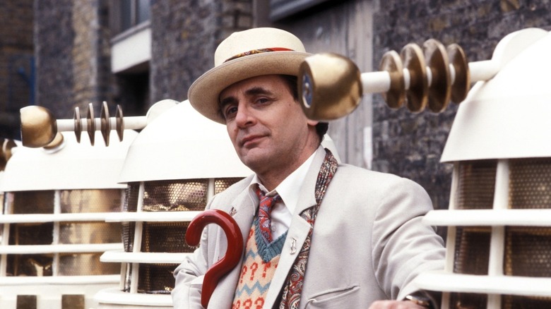 The Seventh Doctor (Sylvester McCoy) poses in a row of Daleks in Doctor Who