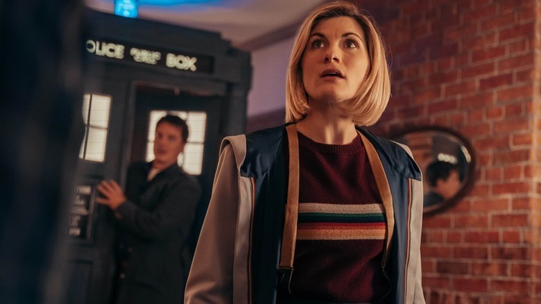 The Thirteenth Doctor (Jodie Whittaker) looks up while the TARDIS sits behind her in Doctor Who