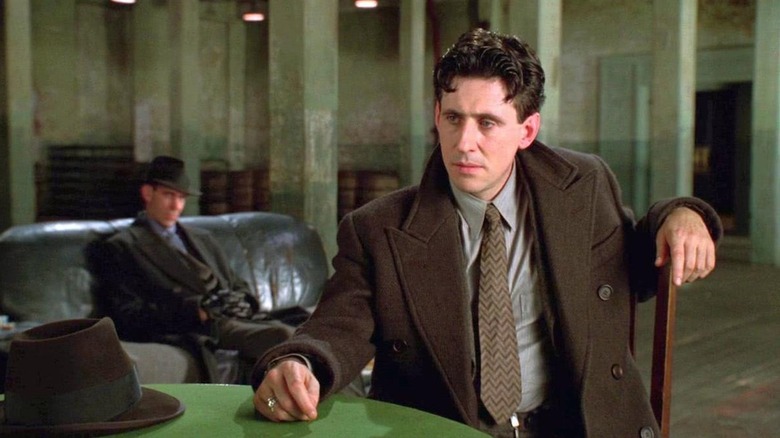 Gabriel Byrne as Tom Reagan, sitting at a table with a man behind him in Miller's Crossing