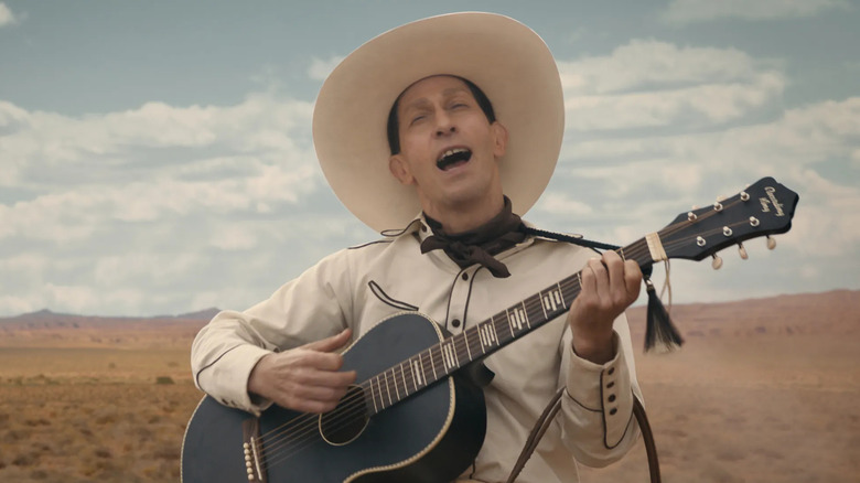 Tim Blake Nelson as Buster Scruggs, strumming a guitar in the desert in The Ballad of Buster Scruggs