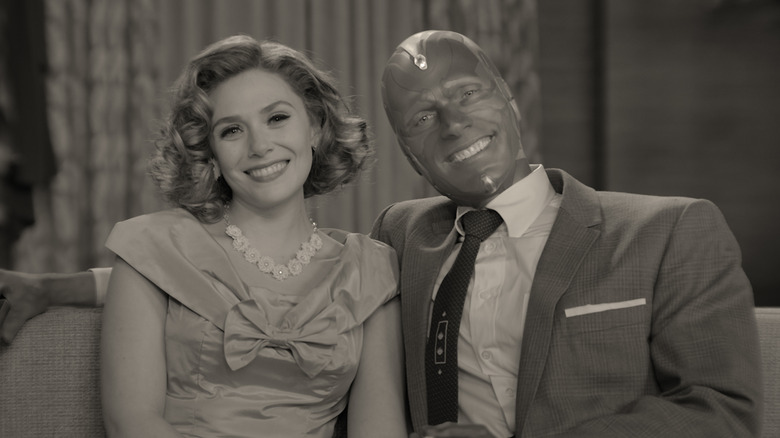 Elisabeth Olson and Paul Bettany as Wanda and Vision, sitting on a couch together smiling in black and white on WandaVision