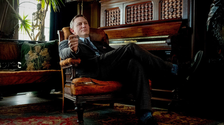 Benoit Blanc lounging in a chair in the Thrombey house in Knives Out