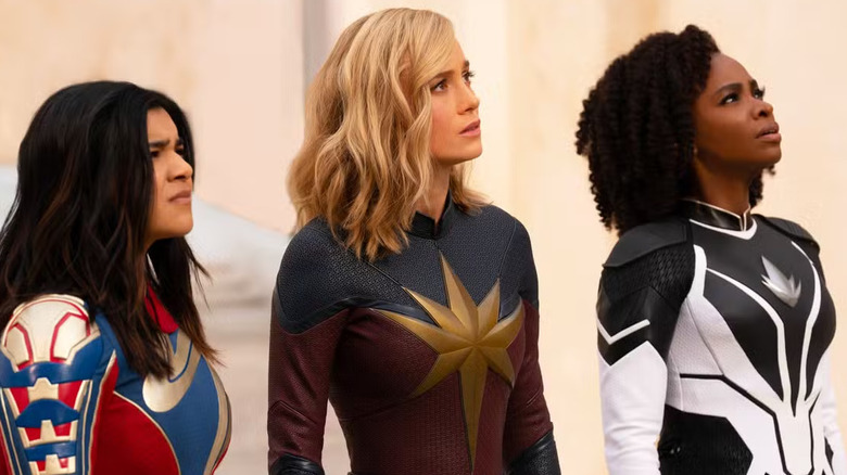 The Marvels (Iman Vellani, Brie Larson, and Teyonah Parris) look to the sky with concern in The Marvels