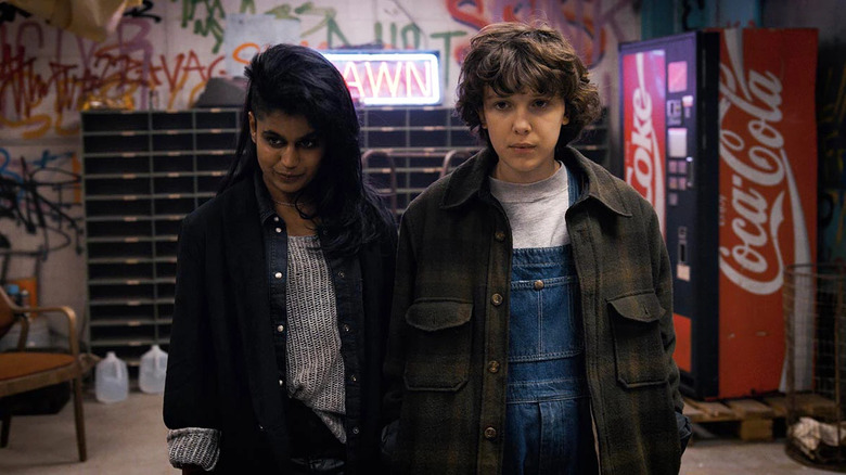 Kali and Eleven standing together in a room full of graffiti in Stranger Things season 2