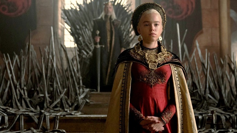 Rhaenyra Targaryen (Milly Alcock) stands in front of the Iron Throne while Viserys I Targaryen (Paddy Considine) watches in House of the Dragon