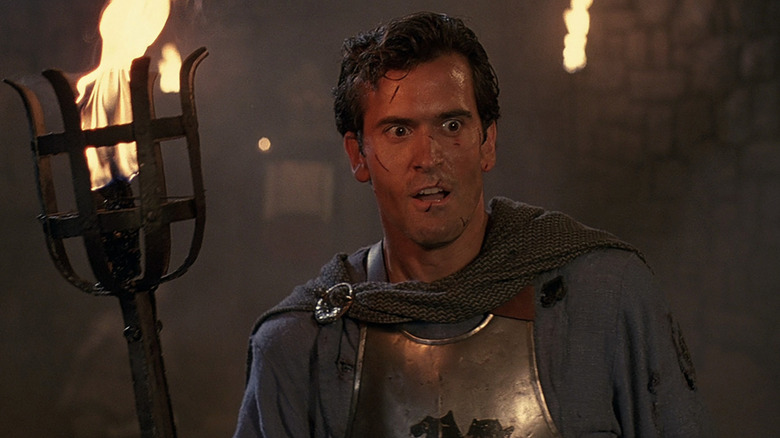 Bruce Campbell as Ashley "Ash" J. Williams tolding a torch and weaing medieval armour with cuts on his face in Army of Darkness