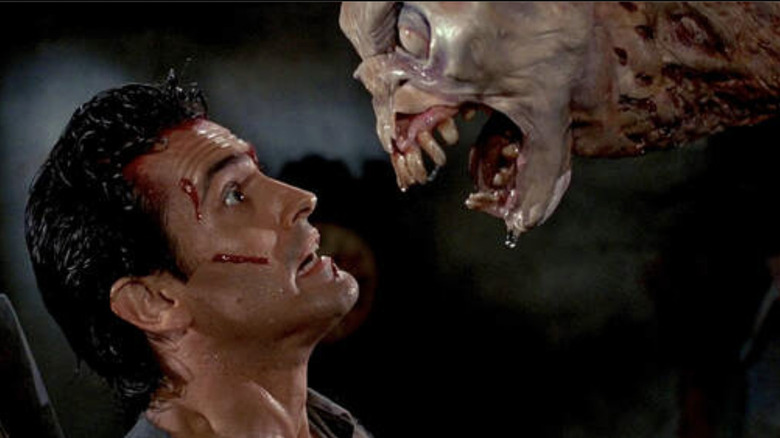 Bruce Campbell as Ash Williams with a cut face looking scared into the eyes of a deadites with its mouth wide open in Evil Dead II