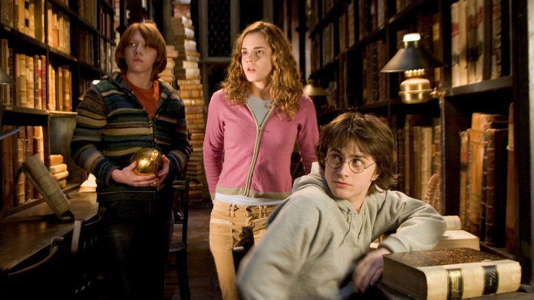Ron Hermione and Harry looking at something in the Hogwarts library in Harry Potter and the Goblet of Fire