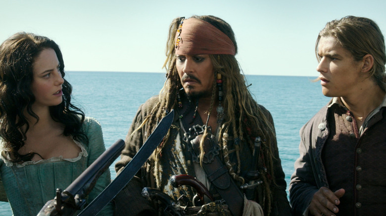 Kaya Scodelario as Carina and Brenton Thwaites as Henry staring at Johnny Depp as Jack Sparrow as he has a sword at his neck in Pirates of the Caribbean: Dead Men Tell No Tales