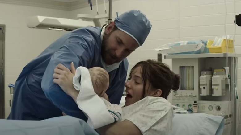 Bradley Cooper as Chris Kyle and Sienna Miller as Taya Kyle holding a baby in American Sniper