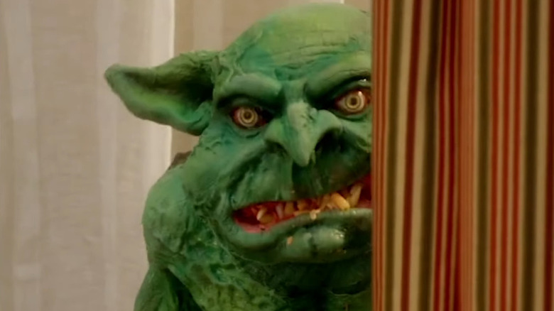 The Cheddar Goblin peeking out from behind a curtain in Mandy