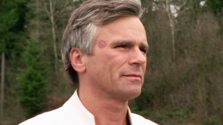 Richard Dean Anderson as Jack O'Neill looks off into the distance with trees visible in the background in Stargate SG-1