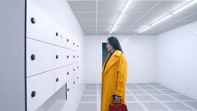Elisabeth in her yellow coat staring at lockers in The Substance