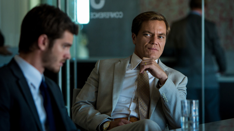 Michael Shannon as Rick looking sternly at Andrew Garfield's Dennis at the conference table in 99 Homes