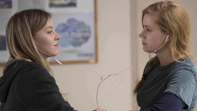Camille (Amy Adams) and Alice (Sydney Sweeney) face each other, sharing iPod earbuds in one ear, with soft, satisfied expressions in Sharp Objects