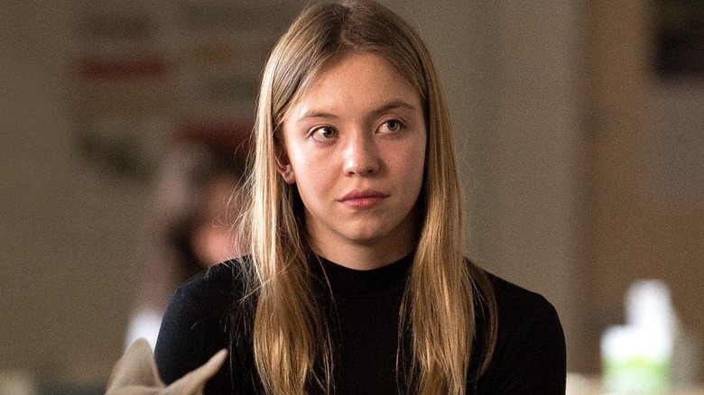 Alice (Sydney Sweeney) looks off to the right side, with tears in her eyes and frowning, wearing a black sweater against a blurred background in Sharp Objects