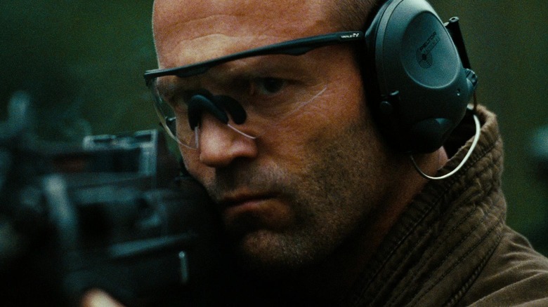Jason Statham as Arthur Bishop wearing headphones while firing a gun in The Mechanic