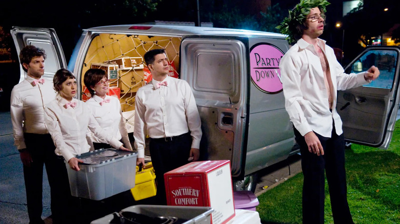 Roman wears a green roman crown on his head as he stares off in tragic suffering and his shirt unbuttoned as his coworkers Henry, Ron, Casey and Lydia watch with bemusement in "Party Down"