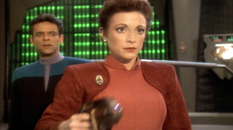 Major Kira raising a phaser while Dr. Bashir looks on in Star Trek: Deep Space Nine