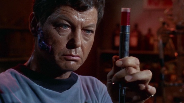Dr. McCoy holdng up a vial of medicine, a lesion on his cheek, on Star Trek