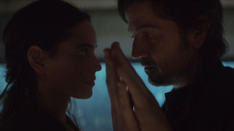 Bix and Cassian touching hand sin their Coruscant apartment at night in Andor season 2