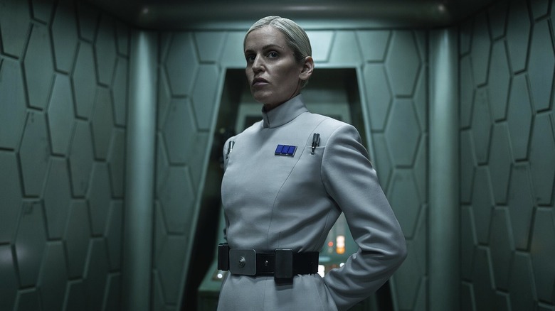 Dedra Meero standing tall and looking stern in a dimly lit corridor in Andor season 2