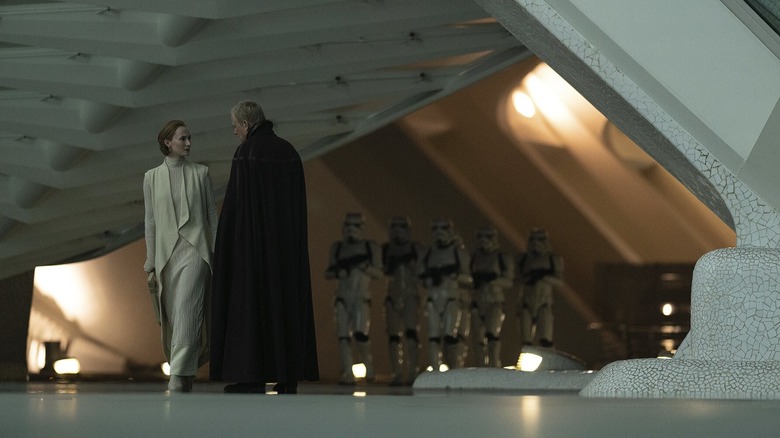 Luthen talking to Mon Mothma on Coruscant while a squad of Stormtroopers walks by in the background in Andor season 2