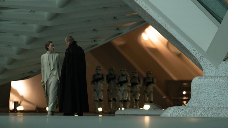 Genevieve O'Reilly as Mon Mothma and Stellan Skarsgård as Luthen Rael talking furtively in front of Stormtroopers in Andor season 2