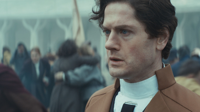 Kyle Soller as Syril Karn appearing shell-shocked in the midst of a riot in Andor season 2